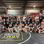 Wrestlers and coaches gathered on a wrestling mat for a group photo.